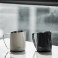 Weißes und schwarzes IKAPE Kännchen nebeneinander auf einem weißen Tisch im Fensterlicht
