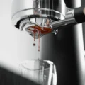 Nahaufnahme: Espresso läuft in zwei Strahlen aus der Unterseite des Siebs, darunter ein Glas