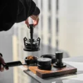 Hand hebt das V3 WDT-Tool über Tamper und Distributor des Sets und einen Siebträger mit klumpigem Kaffeemehl