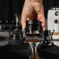 Distributor wird von einem Edelstahl-Siebträger mit Kaffeemehl abgehoben, links und rechts WDT-Tool und Tamper