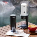 Schwarze und weiße K1 tragbare Espressomaschine auf einem Holztisch am Wasser, die weiße auf einem Ständer