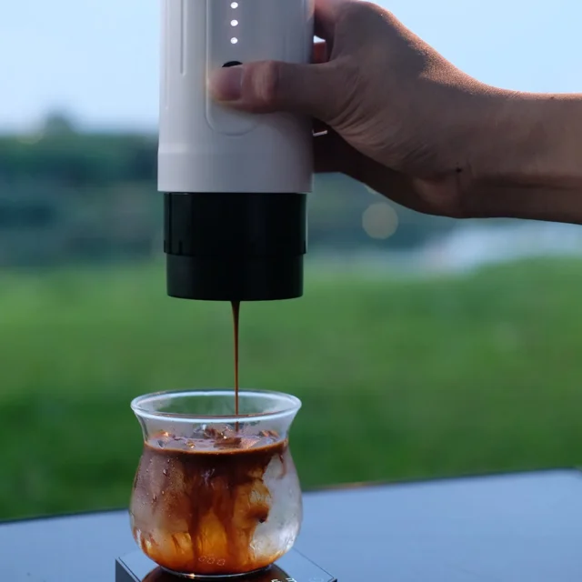 IKAPE Kapo K1 tragbare Espressomaschine in Weiß, in einer Hand, gießt draußen einen Shot in ein Glas mit Eis