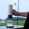 Hand gießt einen Shot aus der weißen IKAPE K1 in ein Glas mit Eis auf einem Campingtisch neben einer Laternenstange