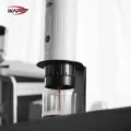 Weiße tragbare Espressomaschine im schwarzen Ständer, ein Espressostrahl füllt einen Glasbecher