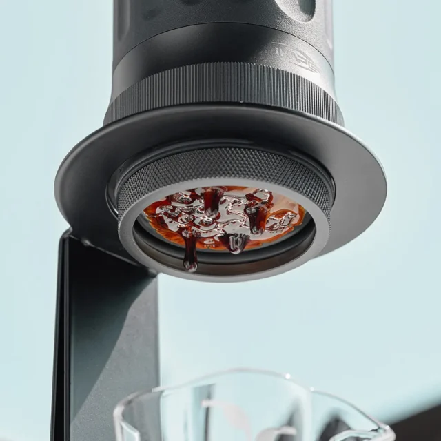 Ansicht von unten: tragbare Espressomaschine im Ring des Ständers, Espresso sammelt sich unter dem offenen Sieb