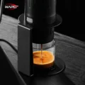 Nahaufnahme von unten auf Stütze und Ring mit schwarzer Maschine, Espresso läuft in ein Glas auf der Basis