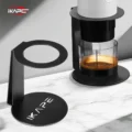 Zwei Ständer auf Marmor, einer leer, einer hält eine weiße tragbare Maschine über einem Glas Espresso