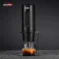 Seitenansicht des Ständers mit schwarzer tragbarer Maschine, Espresso füllt ein Glas, auf dunklem rissigem Stein