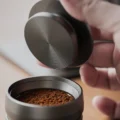 Hand senkt den Tamper der K2, die Stahlfläche mit Ringen zum Sieb voller Kaffeemehl gerichtet