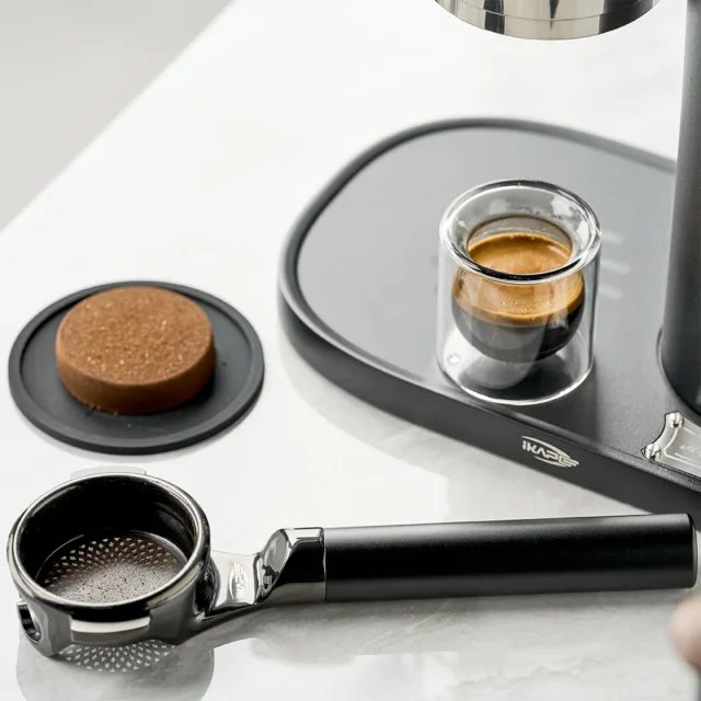 KKLUO Siebträger liegt eben auf seiner flachen Rückseite auf Marmor, neben einem ausgebrühten Puck und einem Espresso