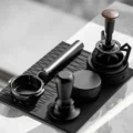 Draufsicht auf den KKLUO Siebträger auf einer schwarzen Matte neben Tamper, Distributor und WDT-Tool