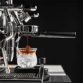 KKLUO Bottomless-Siebträger in einer verchromten Espressomaschine, der Shot läuft auf Eis in einem Glas auf einer Waage