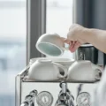 Hand hebt eine blau glasierte Latte-Tasse von einem Stapel Tassen und Untertassen auf einer Espressomaschine