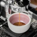 Rosa Latte-Tasse auf einer Waage unter einer Espressomaschine, ein dünner Espressostrahl läuft hinein