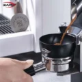 Kaffeemehl fällt aus dem Auswurf einer Mühle in den schwarzen Trichter auf einem Siebträger, oben links der Puck Screen
