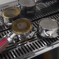 Goldene und silberne Matrix-Siebe in vier Bottomless-Siebträgern auf einer Abtropfschale aus Stahl