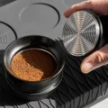 Umgedrehter Tamper mit Metallbasis mit Ringen, neben dem Trichter mit losem Kaffeemehl