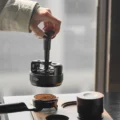 Hand hebt das WDT-Tool am Kopf über ein mit Kaffeemehl gefülltes Siebträgersieb
