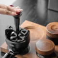Fingerspitzen drücken oben auf das WDT-Tool, das auf einem Siebträger in einem Holztablett sitzt