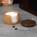 Open filter box full of white paper discs, its dark lid lying beside it next to two coffee beans