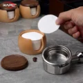 Hand taking one paper filter from the open box, an empty portafilter basket in front