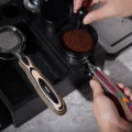 Perlweiß Siebträger in einer schwarzen Station, während eine Hand Kaffeemehl in einem anderen Siebträger umrührt