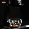 Espresso fällt in einem dünnen Strahl in das Messglas auf einer gerippten schwarzen Matte, vor dunklem Hintergrund