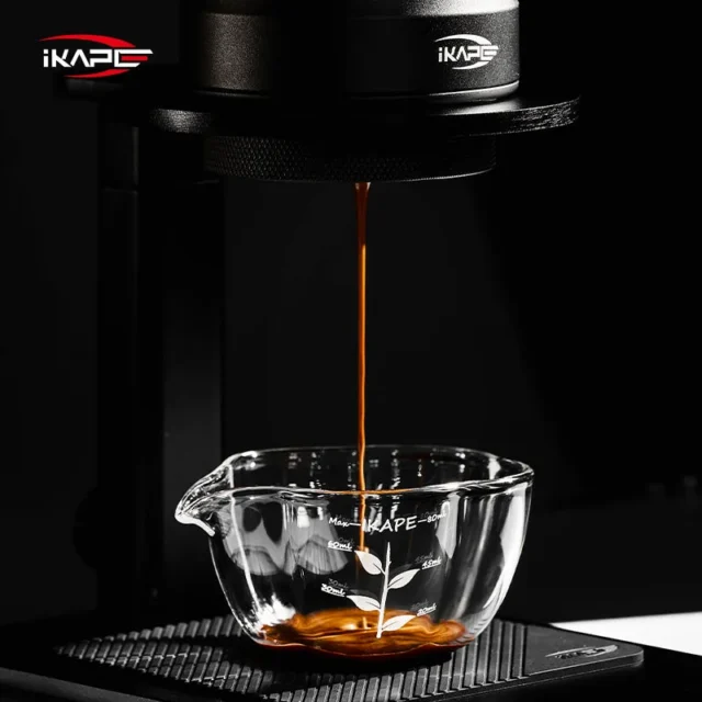 Espresso fällt in einem dünnen Strahl in das Messglas auf einer gerippten schwarzen Matte, vor dunklem Hintergrund