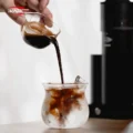 Hand gießt Espresso aus dem Petal Glas in ein beschlagenes Glas mit Eis