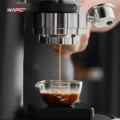 Espresso läuft aus einer verchromten Brühgruppe in das Petal Glas auf einer schwarzen Waage, eine Hand am Siebträger