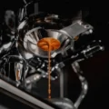 Espresso läuft in einem einzigen Strahl aus dem Boden des konischen Polaris Siebs unter einer verchromten Brühgruppe