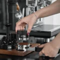 Hand senkt einen schwarzen Distributor auf eine Dosis Kaffee im Polaris Siebträger auf einem Holztablett