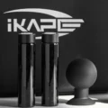 Zwei Bohnenröhrchen aus Glas und ein schwarzer Puck-Bläser vor dem IKAPE Logo
