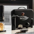 Tragbare Espressomaschine gießt auf Eis, daneben geschlossene IKAPE Tasche, Mühle, Bohnenröhrchen und Puck-Bläser