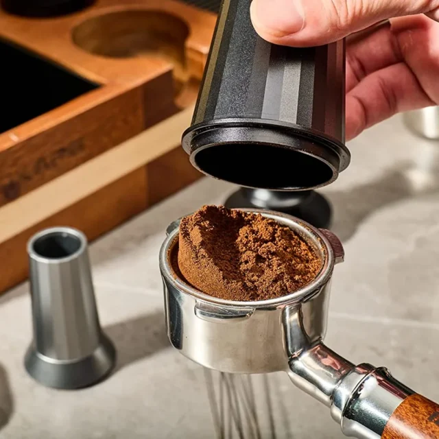 Hand hebt den Dosierbecher von einem Siebträger, im Sieb bleibt eine gehäufte Dosis Kaffeemehl