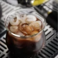 Sense-Glas mit Eiskaffee und Eiswürfeln auf der Abtropfschale einer Espressomaschine