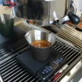 Schwarzer Becher auf einer Digitalwaage fängt unter einem Siebträger an einer Espressomaschine einen Shot auf