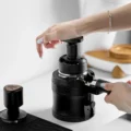 Hand drückt den UniPress auf einen Siebträger in der Gabel einer Mühle, die andere Hand am Griff des Siebträgers