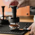 UniPress knapp über einem Siebträger voll lockerem Kaffeemehl, die Stahlbasis kurz vor dem Eintauchen ins Sieb