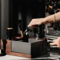 UniPress auf einem Siebträger in einem Holz-Organizer mit grauem Abklopfbehälter, Tamper, Bürste und Trichter
