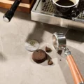 Gewebe-Puck-Screen mit Größe 58,5 mm auf Marmor neben einem ausgeklopften Puck und einem leeren Siebträger