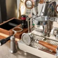 Organizer neben verchromter Espressomaschine, im Loch ein Siebträger mit Kaffee, in einer Aufnahme ein gestreifter Tamper