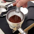 Hand rührt mit einem WDT-Tool durch einen silbernen Dosiertrichter im Kaffeemehl, auf der schwarzen Matte