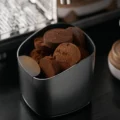 Abklopfbehälter V2 voller ausgebrauchter Espresso-Pucks, vorne auf dem Rand der abgerundete Klopfblock