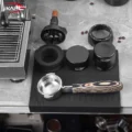 Draufsicht auf die schwarze IKAPE Matte mit Siebträger, Distributor und Tamper neben einer Maschine