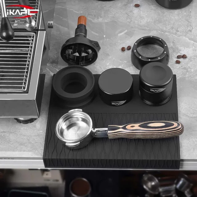 Draufsicht auf die schwarze IKAPE Matte mit Siebträger, Distributor und Tamper neben einer Maschine
