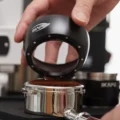 Hand hebt den schwarzen IKAPE Dosiertrichter von einem Siebträger mit gehäuftem Kaffeemehl