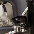Schwarzer IKAPE Dosiertrichter auf einem Siebträger im Halter einer Mühle, Kaffeemehl fällt hinein