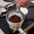 WDT-Tool rührt Kaffeemehl im silbernen IKAPE Dosiertrichter auf einem Siebträger