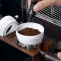 WDT-Tool rührt Kaffeemehl im weißen IKAPE Dosiertrichter, dahinter ein zweiter weißer Trichter auf der Seite